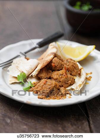 Stock Image - Plate of Goan pork dish with naan bread, lemon slice, coriander and chilli. Fotosearch