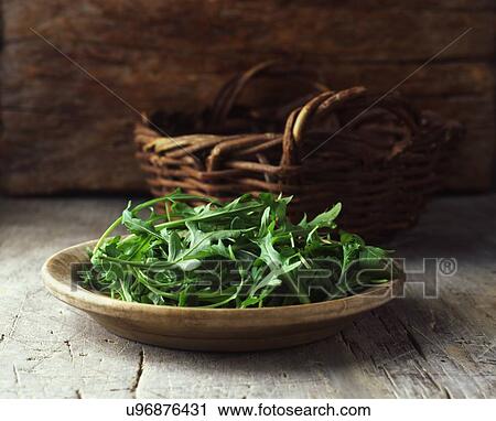 Stock Image - Plate of rocket in wooden bowl and wicker basket. Fotosearch