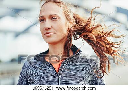 Stock Image - Portrait of female runner with flyaway hair on city footbridge. Fotosearch