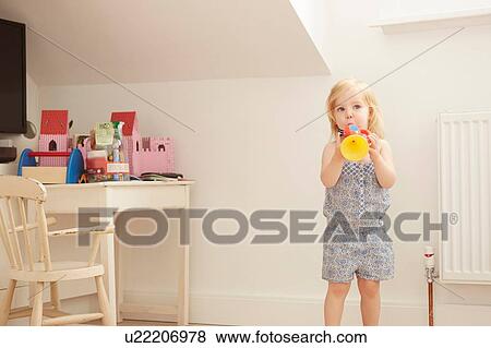 Stock Photo - Portrait of female toddler in playroom playing toy trumpet. Fotosearch