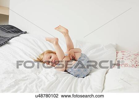 Stock Image - Portrait of female toddler playing on bed. Fotosearch