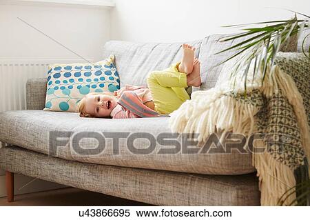 Stock Photography - Portrait of female toddler playing on living room sofa. Fotosearch