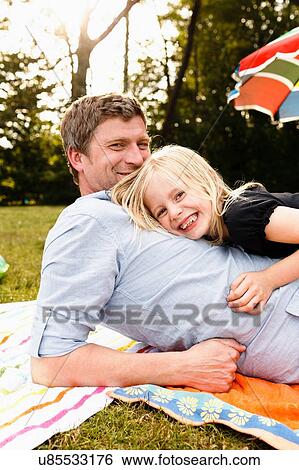 Stock Photograph - Portrait of mature man lying in park with daughter. Fotosearch