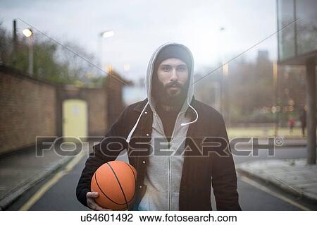Stock Image - Portrait of mid adult man in street, holding basketball. Fotosearch