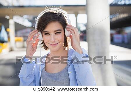 Portrait of mid adult woman adjusting headphones in city View Large Photo Image Stock Image - Portrait of mid adult woman adjusting headphones in city. Fotosearch