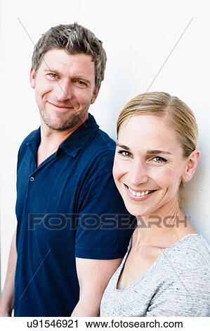 Stock Image - Portrait of mid adult woman and husband leaning against white wall. Fotosearch