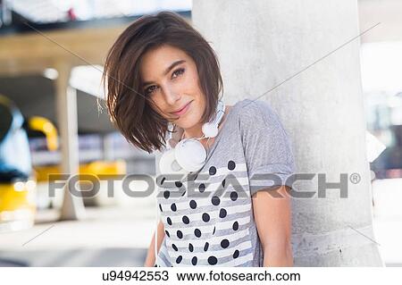 Stock Image - Portrait of mid adult woman leaning against urban pillar. Fotosearch