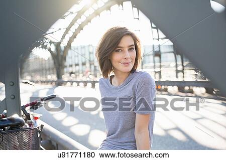 Stock Image - Portrait of mid adult woman on sunlit city bridge. Fotosearch