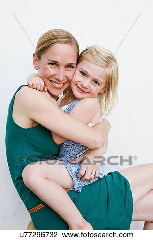 Portrait of mid adult woman with daughter sitting on lap in front of white wall View Large Photo Image Stock Image - Portrait of mid adult woman with daughter sitting on lap in front of white wall. Fotosearch
