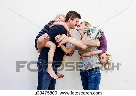 Portrait of parents carrying two young daughters in front of white wall View Large Photo Image Stock Image - Portrait of parents carrying two young daughters in front of white wall. Fotosearch
