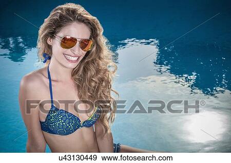 Stock Photo - Portrait of teenage girl with long wavy hair sitting at poolside wearing bikini. Fotosearch
