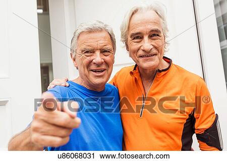 Stock Image - Portrait of two happy senior male runners at front door. Fotosearch