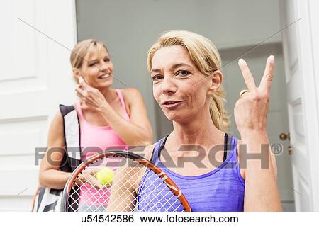 Stock Photograph - Portrait of two mature female tennis players, one making two finger gesture. Fotosearch