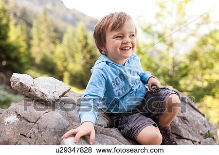 Stock Photo - Portrait of young boy sitting on rock. Fotosearch