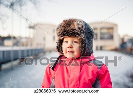 Stock Photograph - Portrait of young girl wearing red anorak and fur trapper hat in snow, Reykjavik, Iceland. Fotosearch