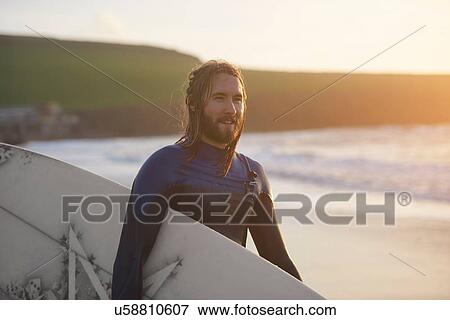 Portrait of young male surfer carrying surfboard on beach, Devon, England, UK View Large Photo Image Stock Photo - Portrait of young male surfer carrying surfboard on beach, Devon, England, UK. Fotosearch