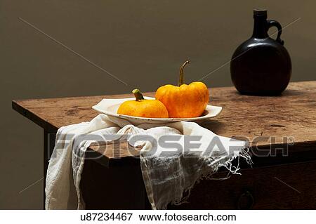 Stock Photo - Pumpkins in serving dish on table with brown glass bottle. Fotosearch