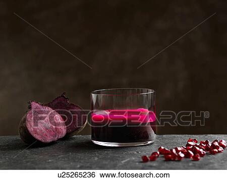 Stock Photograph - Purple raw beetroot and apple juice, halved beetroot and pomegranate seeds. Fotosearch