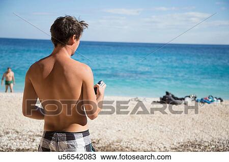 Stock Image - Rear view of bare chested young man on beach, Golfo di Orosei, Sardinia, Italy. Fotosearch