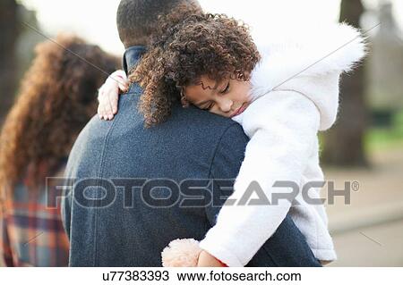 Stock Image - Rear view of father carrying sleeping daughter. Fotosearch