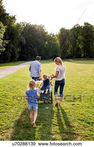 Stock Photo - Rear view of parents and three girls strolling in park. Fotosearch