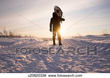 Stock Photo - Rear view of silhouetted man carrying snow shoes on shoulders in snowy landscape, Ural, Russia. Fotosearch