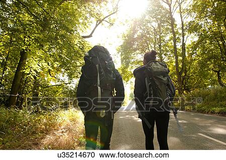 Stock Image - Rear view of young hiking couple on rural road. Fotosearch