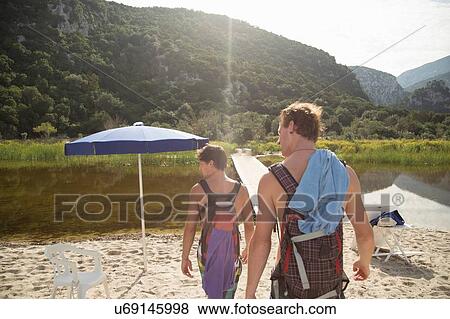 Stock Photo - Rear view of young men carrying backpacks on beach, Cala Luna, Sardinia, Italy. Fotosearch