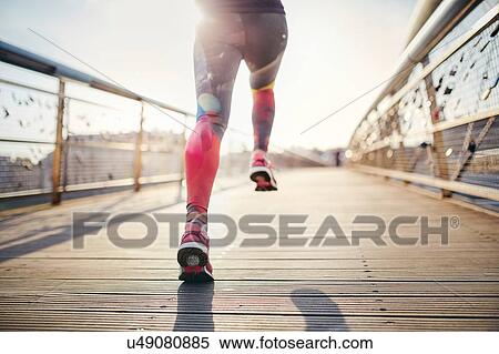 Stock Photography - Rear waist down view of female runner running across footbridge. Fotosearch