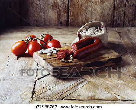 Stock Photo - Roma tomatoes on the vine, chorizo and butter beans in burlap sack on wooden cutting board. Fotosearch