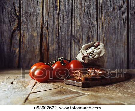 Stock Image - Roma tomatoes on vine, chorizo and butter beans in burlap sack on wooden cutting board. Fotosearch