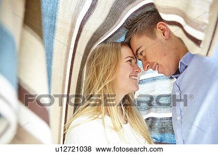 Stock Photo - Romantic young couple covered in a blanket. Fotosearch