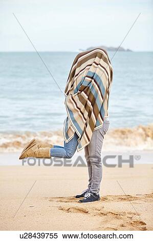 Stock Photography - Romantic young couple covered in blanket on beach, Constantine Bay, Cornwall, UK. Fotosearch