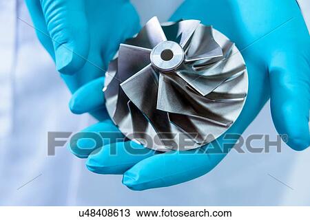Stock Image - Scientist in automotive research laboratory holding turbo charger turbine, close up. Fotosearch