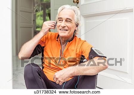 Picture - Senior male runner at front door preparing earphone music. Fotosearch