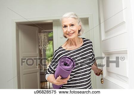 Stock Photography - Senior woman at front door carrying yoga mat. Fotosearch