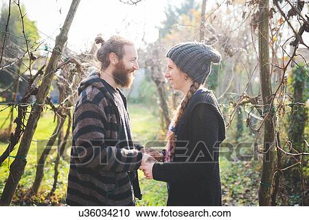 Stock Image - Side view of couple among trees face to face, holding hands, smiling. Fotosearch