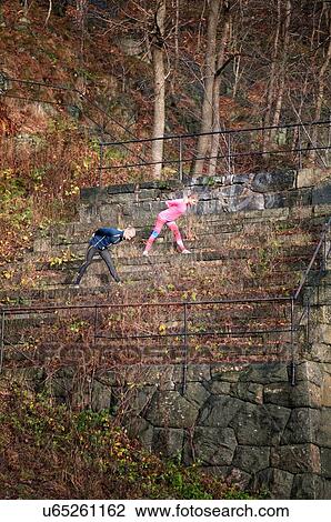 Stock Image - Side view of couple doing stretching exercises on overgrown stone steps. Fotosearch