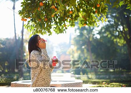 Side view of mature woman blowing bubbles under orange tree, Seville, Spain View Large Photo Image Stock Photo - Side view of mature woman blowing bubbles under orange tree, Seville, Spain. Fotosearch