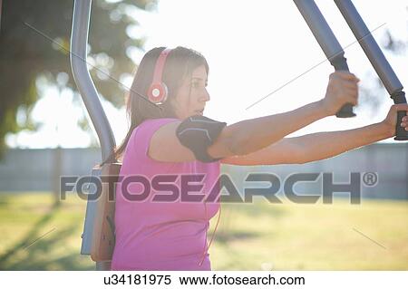 Side view of mature woman wearing headphones using outdoor pec deck View Large Photo Image Stock Photography - Side view of mature woman wearing headphones using outdoor pec deck. Fotosearch