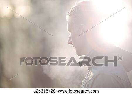 Stock Photo - Side view of mid adult man looking away, condensation from breath. Fotosearch