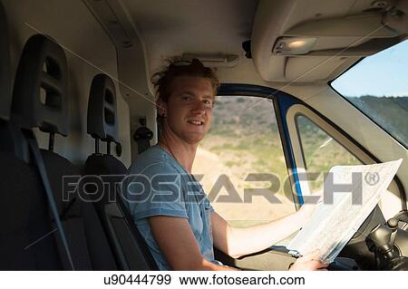 Side view of young man sitting in van holding map looking at camera smiling, Costa Smeralda, Sardinia, Italy View Large Photo Image Stock Photo - Side view of young man sitting in van holding map looking at camera smiling, Costa Smeralda, Sardinia, Italy. Fotosearch