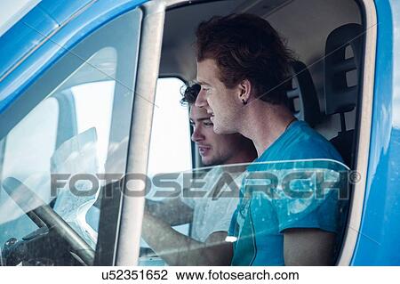 Stock Image - Side view of young men in van looking at map, Costa Smeralda, Sardinia, Italy. Fotosearch