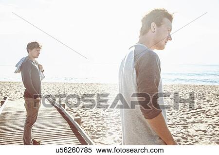 Side view of young men on wooden pier on beach in front of ocean looking away, Costa Smeralda, Sardinia, Italy View Large Photo Image Stock Photography - Side view of young men on wooden pier on beach in front of ocean looking away, Costa Smeralda, Sardinia, Italy. Fotosearch