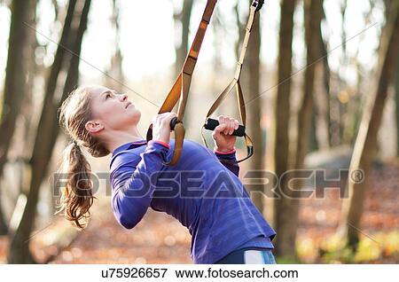 Stock Photo - Side view of young woman bending over backwards using resistance bands. Fotosearch