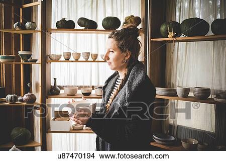 Side view of young woman holding ceramic dish in front of shelves displaying clay pots and pumpkins View Large Photo Image Picture - Side view of young woman holding ceramic dish in front of shelves displaying clay pots and pumpkins. Fotosearch