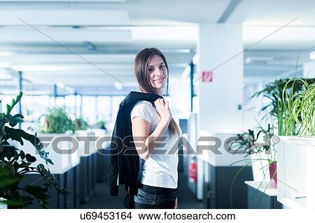 Side view of young woman in office carrying jacket over shoulder looking at camera smiling View Large Photo Image Picture - Side view of young woman in office carrying jacket over shoulder looking at camera smiling. Fotosearch