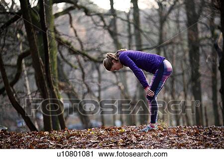 Stock Image - Side view of young woman wearing sports clothing bending over hands on knees, exhausted. Fotosearch