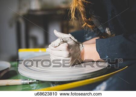 Stock Image - Side view of young womans hands shaping clay on pottery wheel. Fotosearch