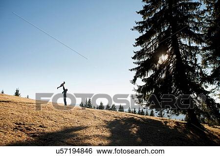 Stock Photograph - Silhouette of man holding up toddler daughter on hill, Tegernsee, Bavaria, Germany. Fotosearch